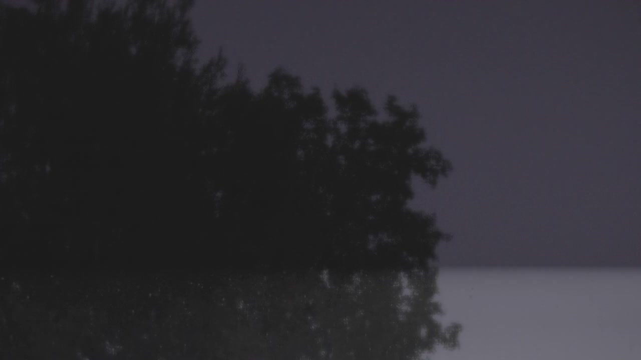 Uma pequena casa rural fica na floresta densa à noite durante uma forte tempestade de chuva, iluminada por súbitos clarões de relâmpagos.