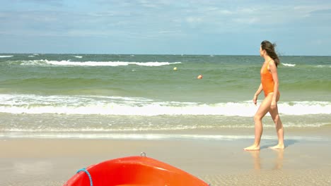 chica con traje de baño naranja de una pieza en una hermosa playa mirando al agua a las olas rompiendo mientras está de vacaciones