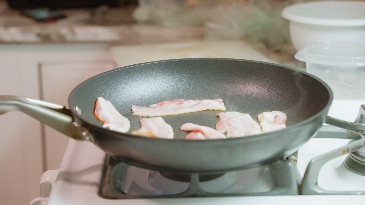 Bacon che frigge ed emette vapore a fiamma bassa in una padella di Teflon