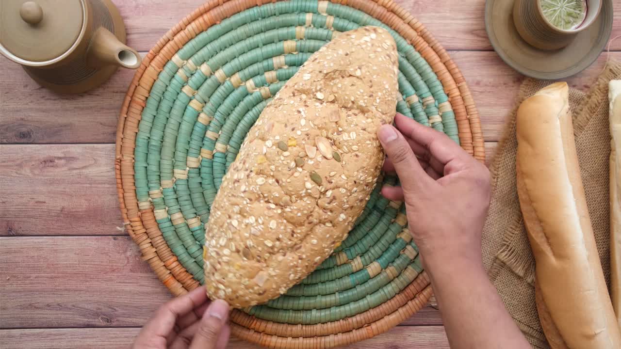 manos sosteniendo un gran pan de varios granos en un plato decorativo