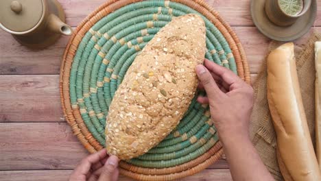 hands holding a large loaf of multigrain bread on a decorative plate