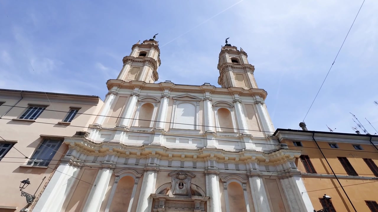 Vista dal basso dell'ex chiesa di San Francesco di Paola a Parma, Italia, che evidenzia la sua facciata barocca simmetrica, i campanili gemelli e i dettagli architettonici ornati.