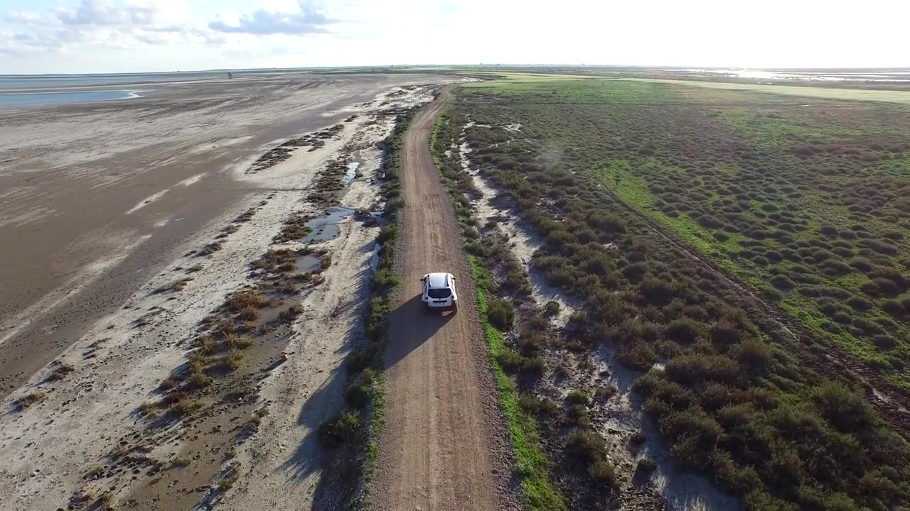 Vista aerea di un SUV che guida su una strada sterrata attraverso un paesaggio costiero