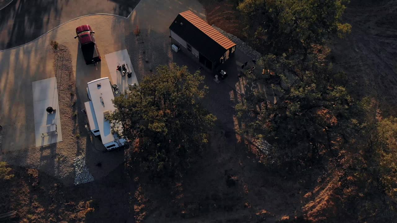 Aerial pull back shot of an RV Trailer in an RV Park at sunset showing the setting sun.