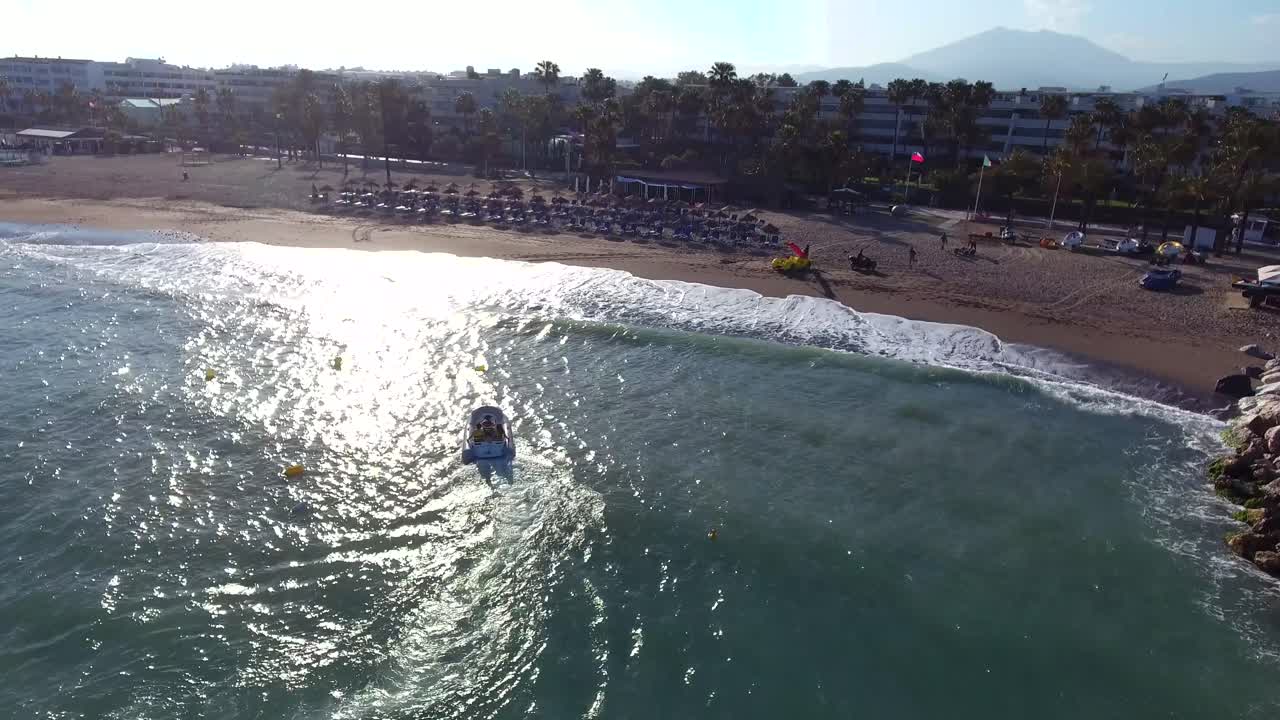 piccola barca che arriva a riva durante un tramonto filmato da drone in 4k a marbella, malaga spagna