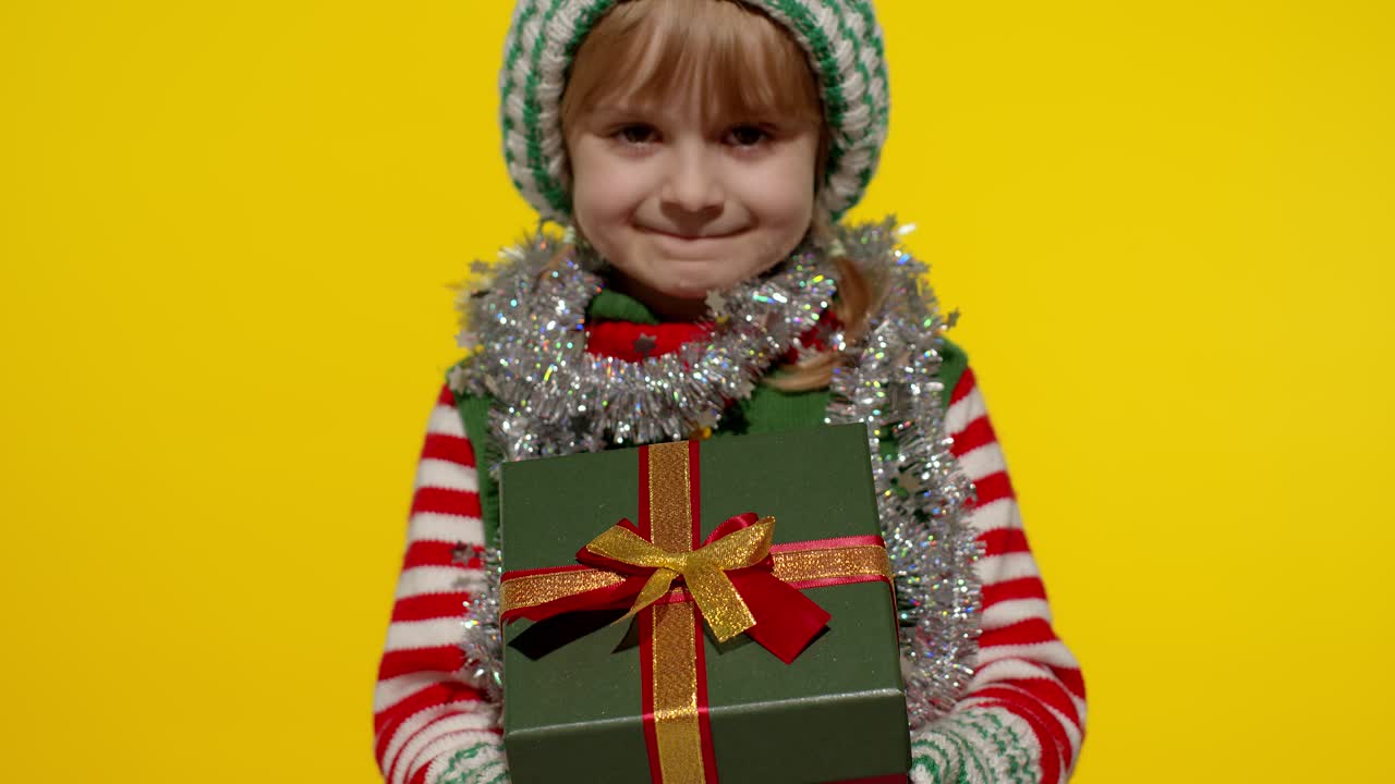 Dívka jako vánoční skřítek, pomocník Santa Clause, dává dárkovou krabici do kamery. Šťastné novoroční svátky.
