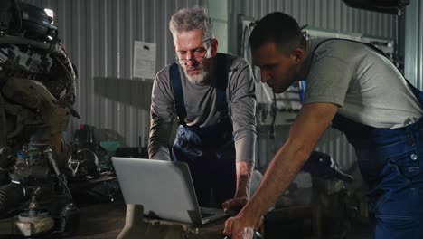 two mechanics inspecting a car engine using a laptop