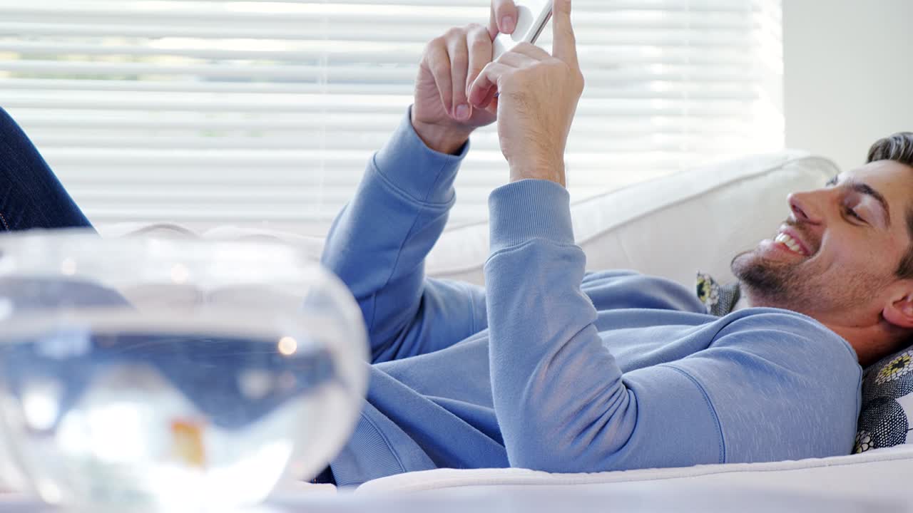 금색 물고기 그 ⁇ 과 소파에 누워있는 남자가 모바일 4k 4k를 사용하고 있습니다.