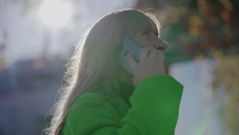 mujer madura con chaqueta verde hablando en el teléfono inteligente al aire libre