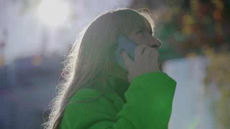 mature woman wearing green jacket talking on smartphone outdoor