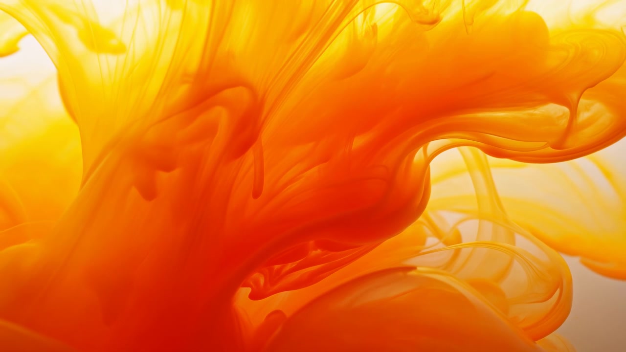 Vista macro di liquido arancione e giallo simile a inchiostro che forma pennacchi vorticosi e volute stratificate in un fluido traslucido. La calda retroilluminazione crea morbidi riflessi