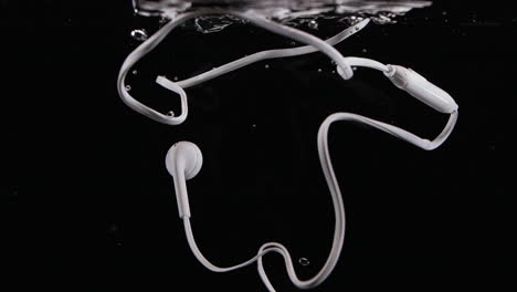 old wired headphones drop in water with bubbles destroyed in slow motion