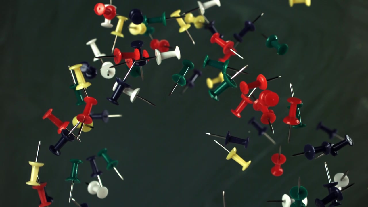 Colorful Pushpins Falling in Slow Motion Against a Dark Background