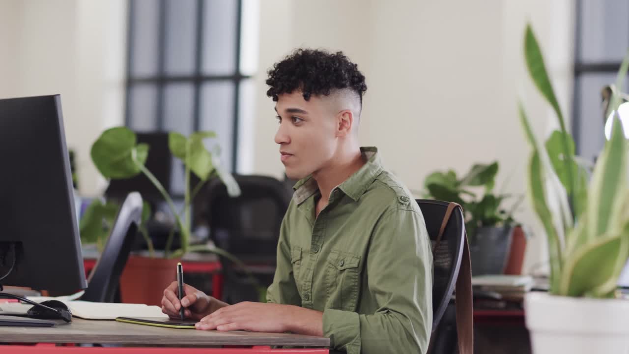Happy biracial male creative using tablet and computer at casual office, in slow motion