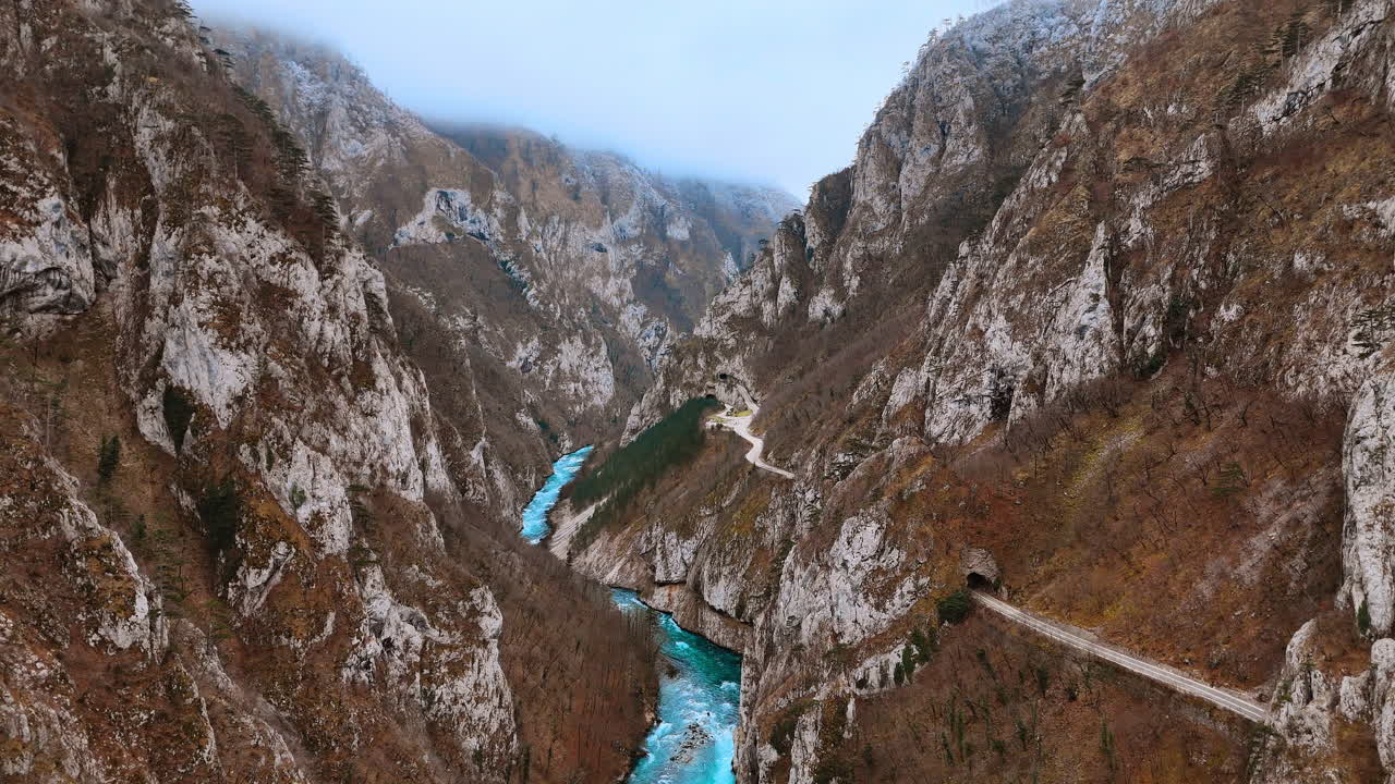 Kanyonda dağ yolu tünellerinin yüksek açılı görünümü. Sisli Piva kanyonunda turkuaz nehirle birlikte sarp kayalıklar arasından geçen tünelli virajlı yolun havadan görünümü.