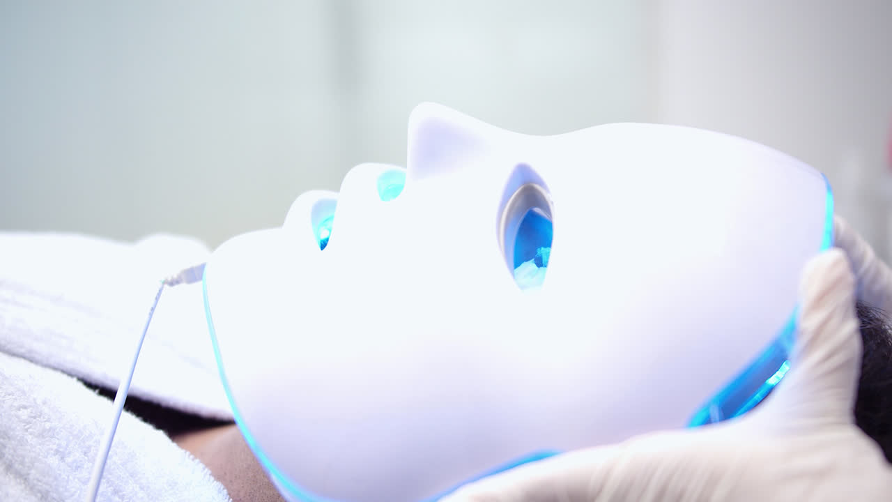 Beautiful slow motion long profile shot of a young man receiving a beauty treatment with a LED mask in a dermatology clinic.