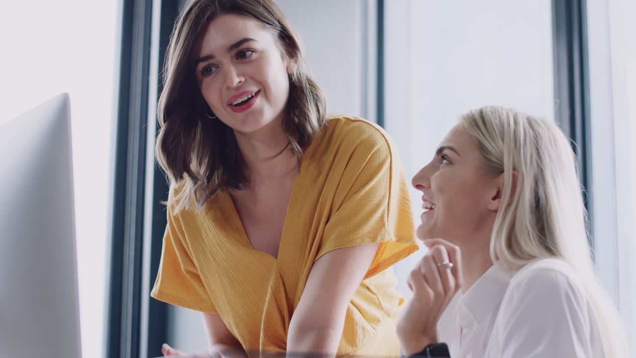 두 명의 백인 여성 동료들이 컴퓨터 화면을 보고 창의적인 프로젝트를 논의하고 있습니다.