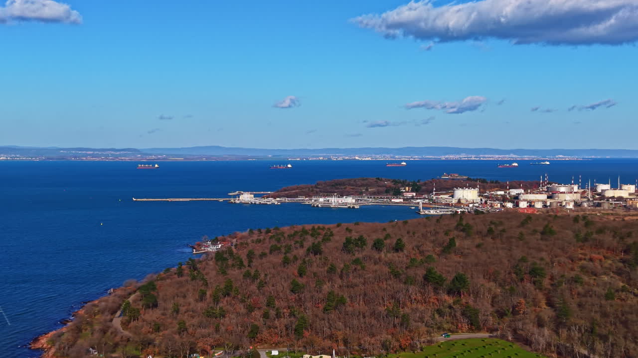 Stort havområde med fjerntliggende land og skip under en klar blå himmel i et kystområde på dagtid.
