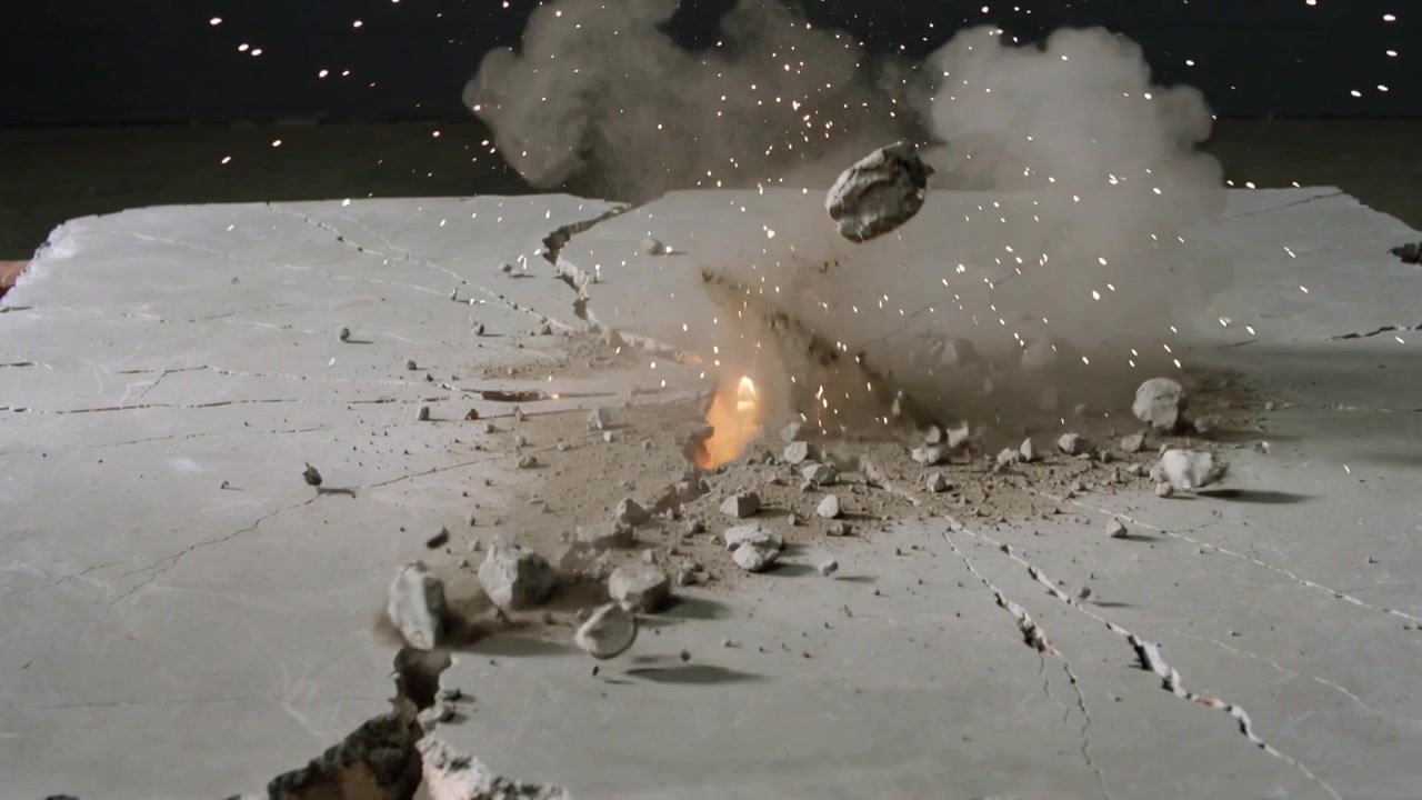 Detonatore centrale in fase di detonazione, lastra di cemento che si incrina ed espelle scintille e frammenti in un laboratorio di prova.