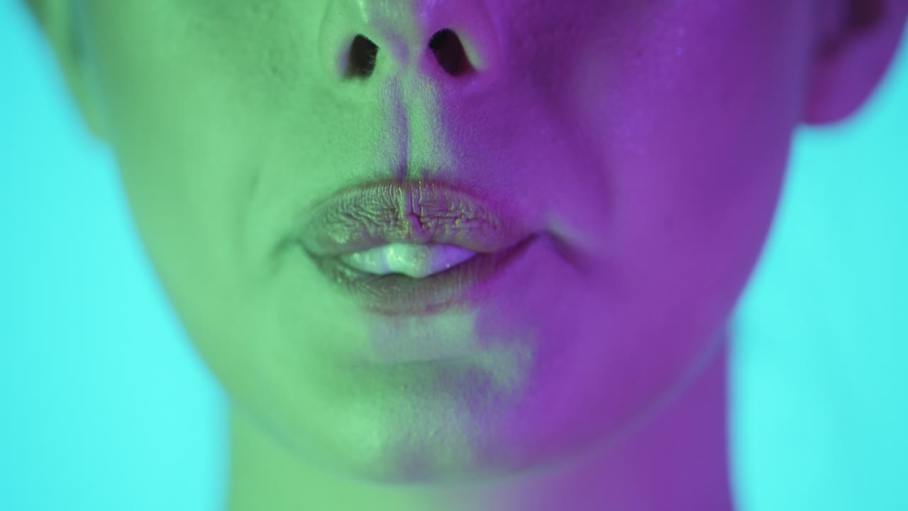 acercamiento extremo de un labio de una mujer masticando un chicle y luego rodando su lengua y haciendo una pequeña burbuja de chicle y sonriendo frente al fondo turquesa en cámara lenta