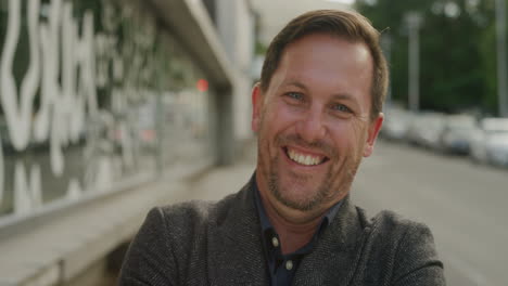 portrrait-of-successful-businessman-smiling-cheerful-at-camera-enjoying-professional-urban-lifestyle-cheerful-male-entrepreneur-in-urban-city-street-arms-crossed