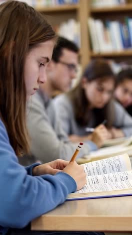 a girl is sitting at a desk with a pencil and a book. she is writing in the book