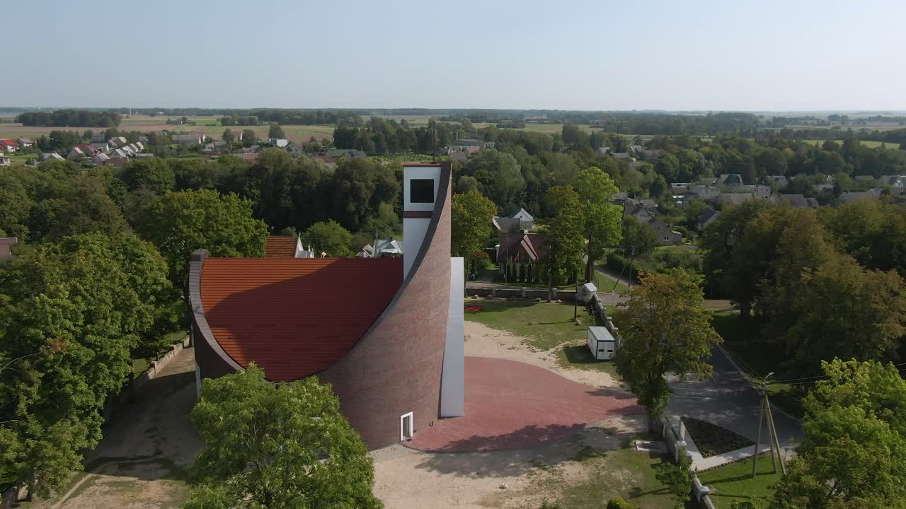 Drone side shot of beautiful red roofed brick church and revealing beautiful small town with trees around of Lithuania, aerial view.