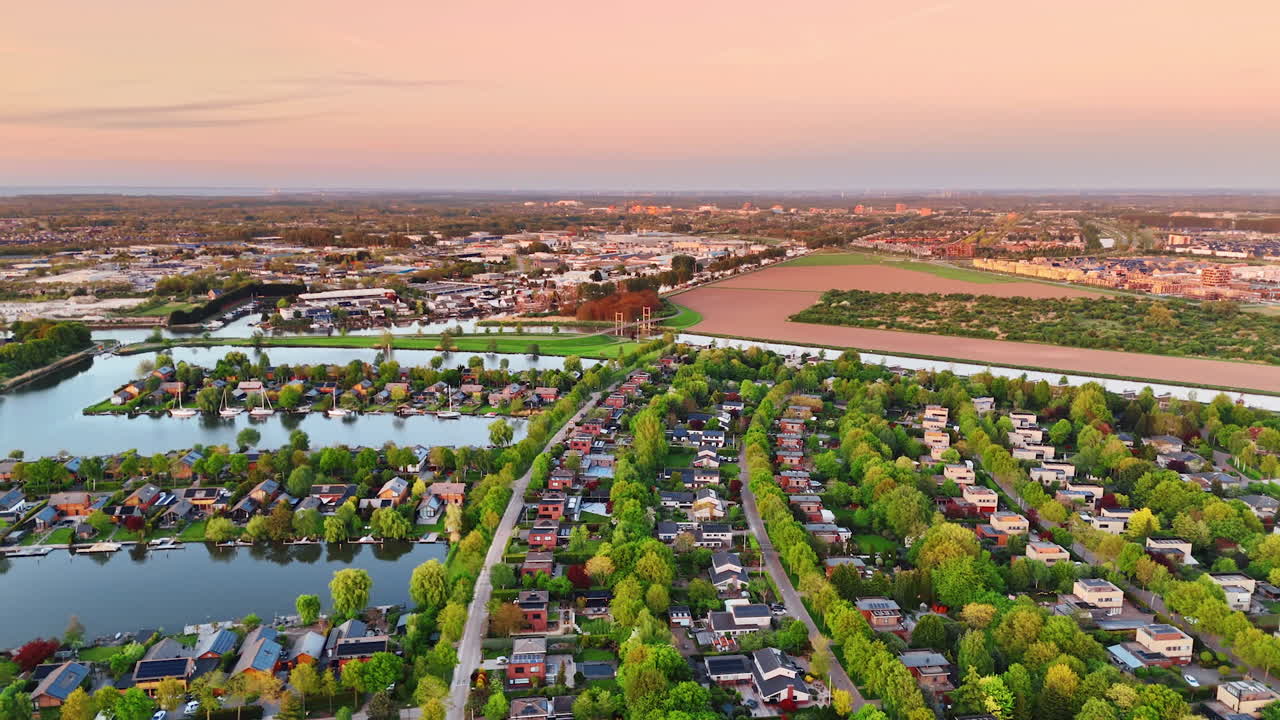 Picturesque village with rows of houses and vegetation. Vast scenery of Holland countryside at sunset. Aerial view.