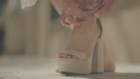 close-up of woman fastening elegant high-heeled sandal. fashion and style concept.