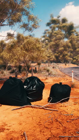 tres bolsas de basura negras se sientan al lado de un camino de tierra en la australia rural