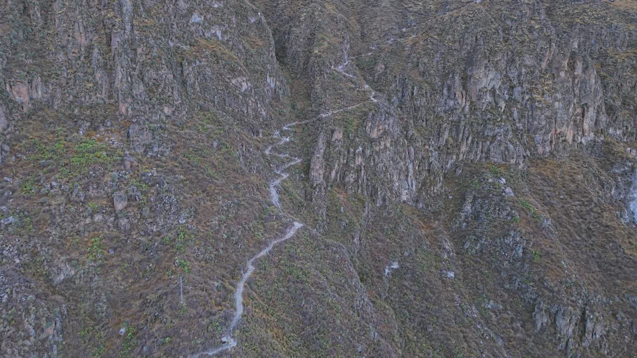 A close-up drone shot begins on the hiking trail itself, then reverses to reveal the vast Colca Canyon, placing the viewer within the landscape and unveiling its awe-inspiring scale