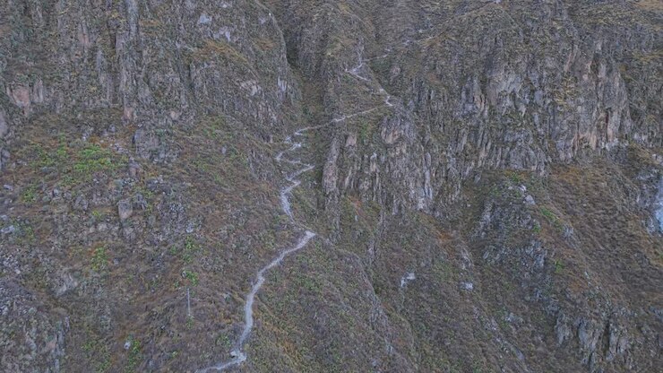 A close-up drone shot begins on the hiking trail itself, then reverses to reveal the vast Colca Canyon, placing the viewer within the landscape and unveiling its awe-inspiring scale