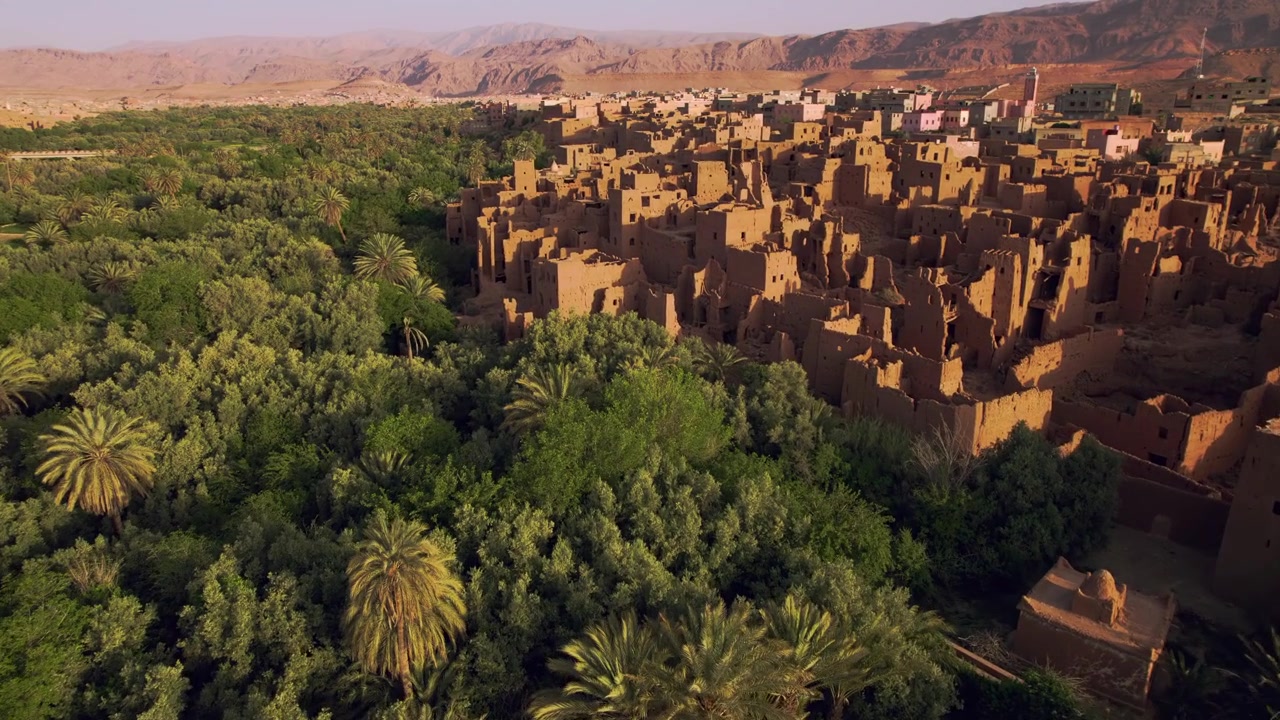 Oasi di Tinghir a Draa-Tafilalet, Marocco sud-orientale, delimitata da palmeti di Phoenix dactylifera, architettura ksar in terra e le colline pedemontane del Jbel Saghro vicino alla Valle del Todgha, ripresa aerea in avanti