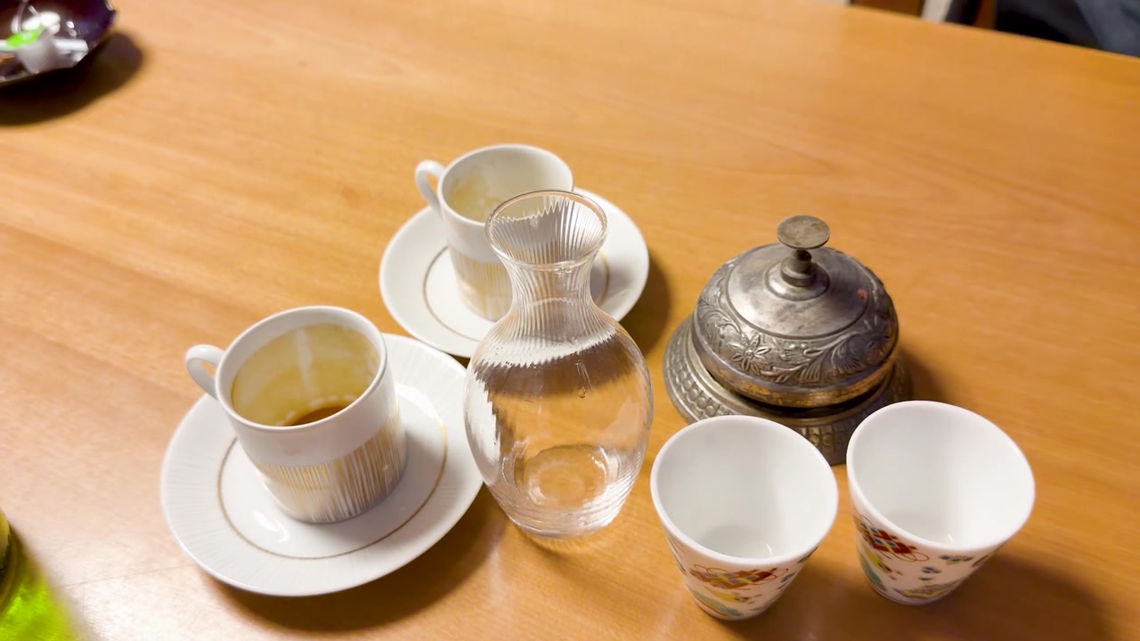 A hand rings a metal service bell on a table with coffee and sake sets