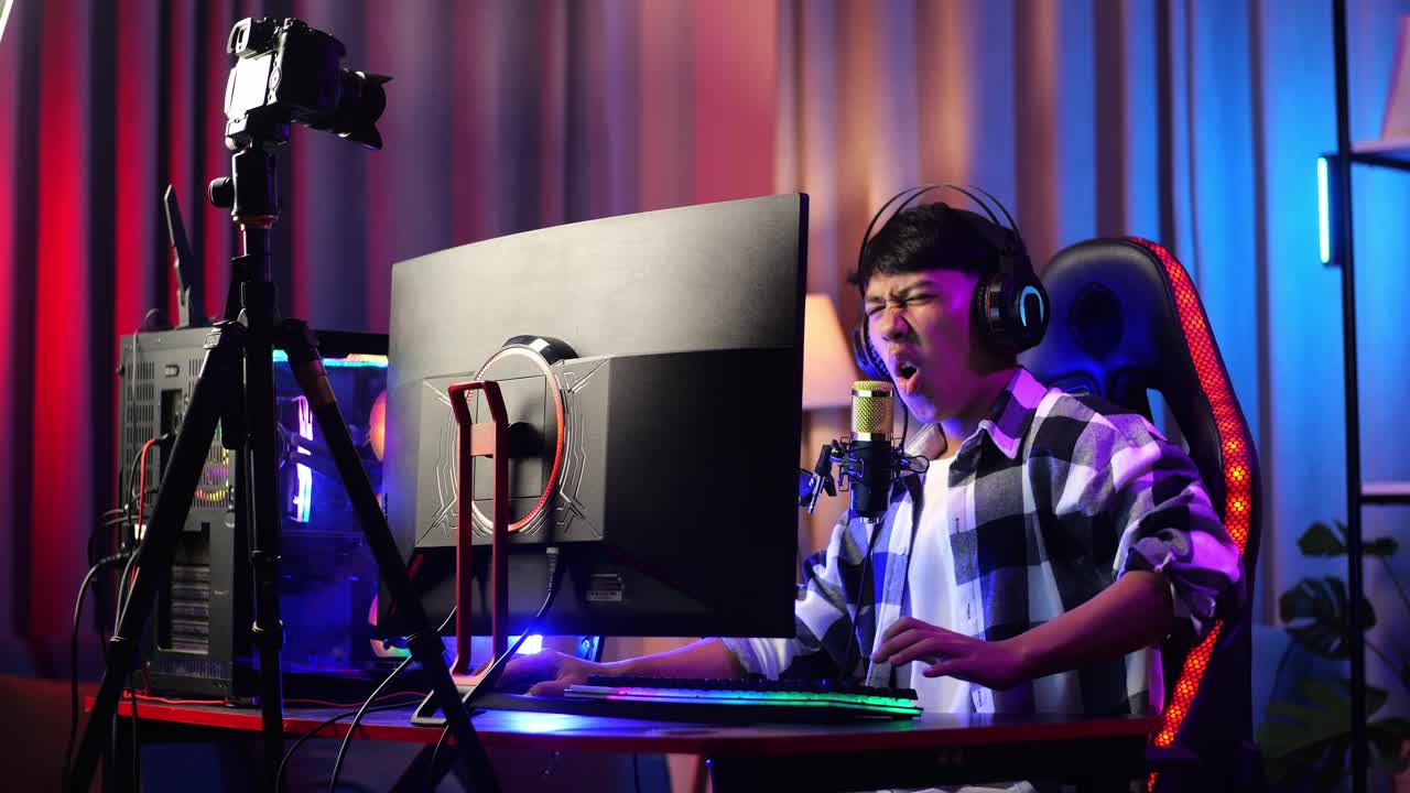 아시안 소년 스트리머는 개인 컴퓨터에서 네트워크를 통해 게임을 할 때 허리 통증이 있습니다. 라이브 스트리밍 비디오 게임, rgb led 스트립 라이트에 의해 조명 된 책상