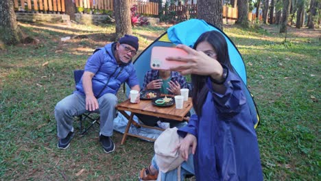 happy asian father and teenage children take a selfie on the phone together at the campground