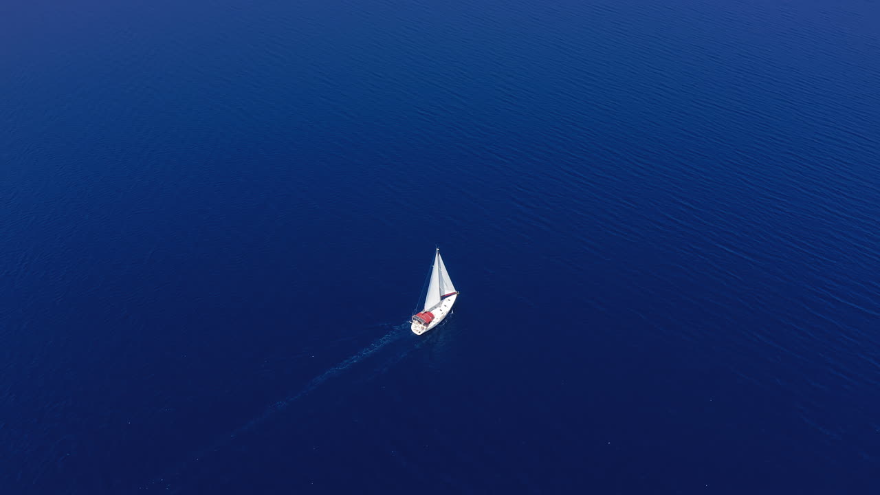 Aerial: A sailboat is sailing in the open calm blue sea