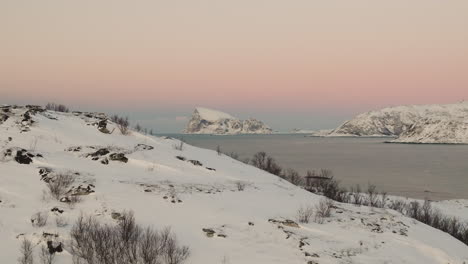 isla haaja cubierta de nieve en el horizonte sobre el fiordo, cielo rosado del atardecer