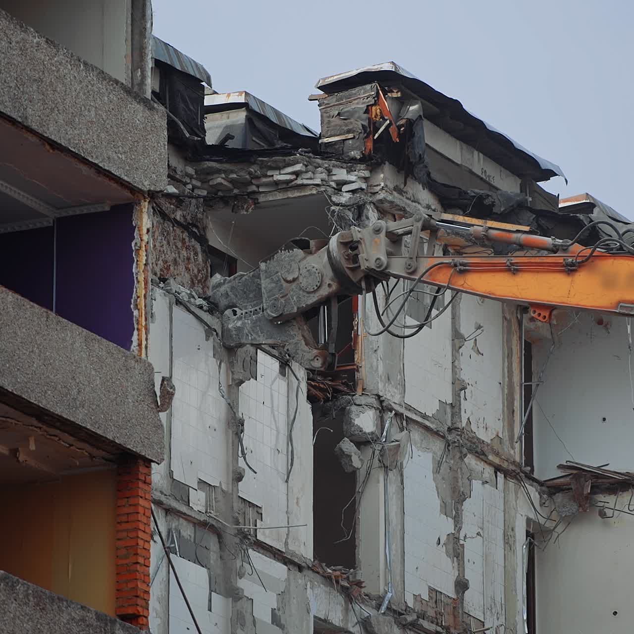 Demolishing machine claw tries to grab the concrete block to tear it off. Excavator working at dismantling the ruined house