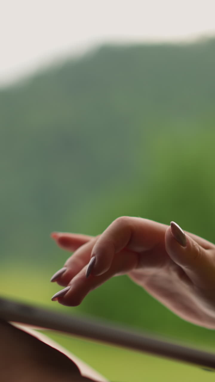 Woman types text on laptop computer keyboard sitting against green mountains silhouette at resort close side view zoom out slow motion
