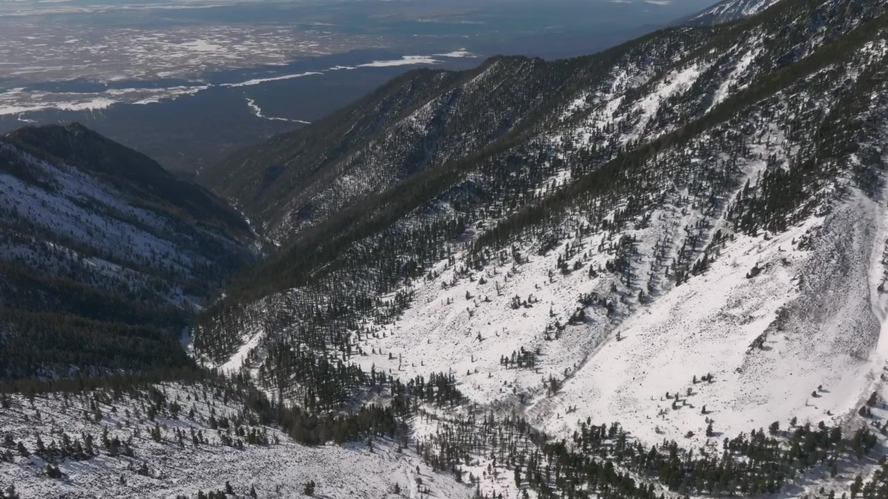 Drone footage of snow covered mountain slopes and conifer forest above a deep valley near Galina Peak, Arshan, Republic of Buryatia, Russia on a clear winter day
