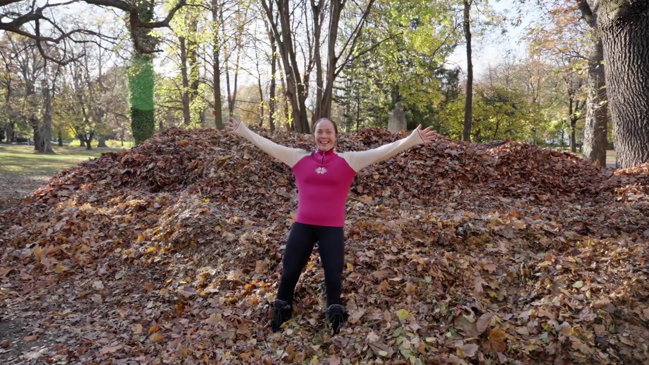 Een lachende vrouw valt in een zachte stapel kleurrijke herfstbladeren in een park, lachend van vreugde