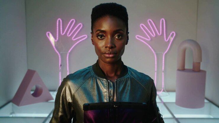 Rotating on cue, model in metal bomber jacket presenting trimmer and clutch in studio, neon hands