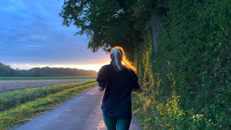 slow motion shot showing silhouette of woman jogging on rural path against sunset light