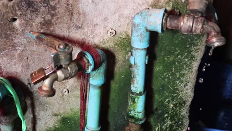 close-up of water dripping from aged blue pipes with visible moss and corrosion.
