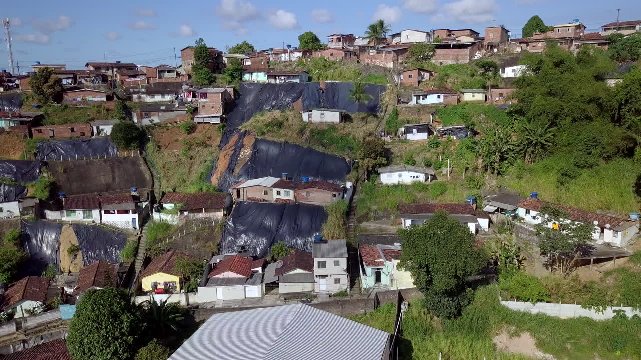 Aerial perspective over the Macaxeira neighborhood hillside in Recife Brazil focusing on the modest dwellings parked cars and protective tarps highlighting the pervasive poverty danger and inequality