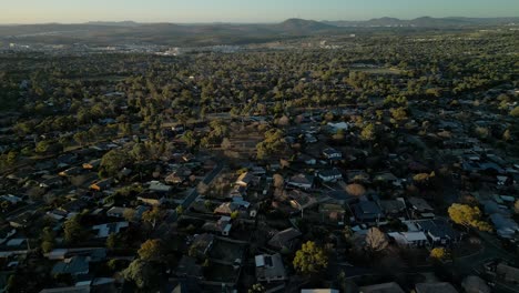 drone flies toward canberra’s skyline, passing rooftops of rivett and distant landmarks glowing in afternoon sun