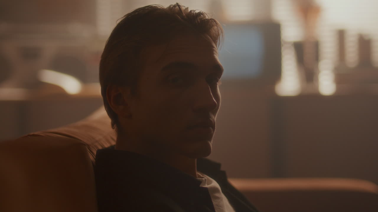 Portrait of Young Handsome Man Sitting on Couch in Softly Lit Room