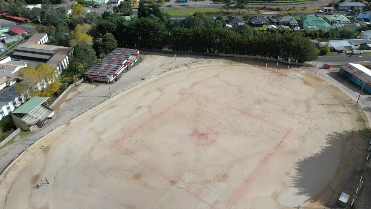 Slow pan out to reveal ground and surrounding community and mountain range - aerial drone shot Queenstown Oval, Tasmania, Australia - famous gravel oval