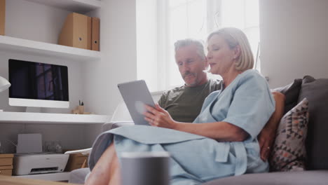 senior couple sitting on sofa at home using digital tablet together